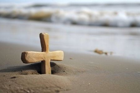 A simple wooden cross rests in the sand, the ocean waves gently lapping in the background.の写真素材