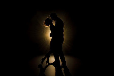 Silhouette of a couple embracing passionately in the dark, illuminated by a warm light.の写真素材