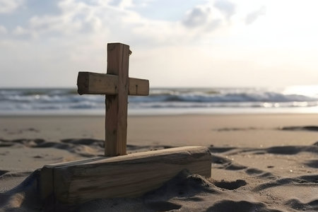 A rustic wooden cross rests on a sandy beach, the ocean gently rolling in the background. The peaceful sunset casts a warm glow.の写真素材