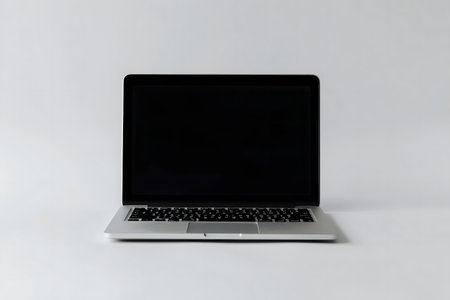 A sleek silver laptop sits on a plain white surface. The screen is black, creating a minimal aesthetic.の写真素材