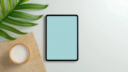 Minimalist flatlay showcasing a tablet with a blank screen, a tropical leaf, and a bowl on a white background.の写真素材