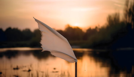 A white flag gently flows in the sunset breeze near a tranquil lake. Peaceful scene.の写真素材