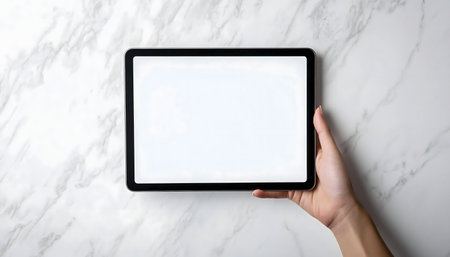 A hand holds a tablet with a blank white screen against a marble background.の写真素材