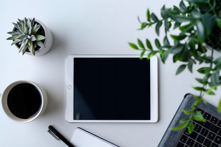 A minimalist workspace featuring a tablet, coffee, plants, and keyboard.の写真素材