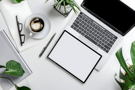 A flatlay image showing a modern workspace setup with a laptop, tablet, coffee, plants, and office...