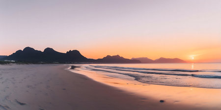 Peaceful sunrise over a sandy beach with mountains in the background.の写真素材