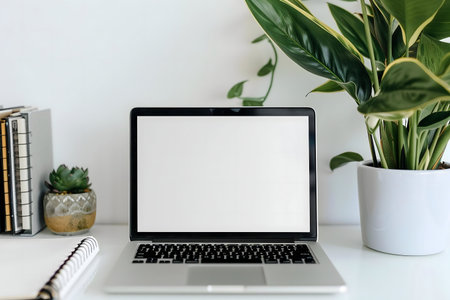 A clean and modern workspace featuring a laptop, houseplants, and notebooks on a white desk.