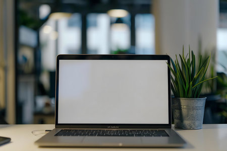 A clean, modern workspace featuring a laptop with a blank screen and a small potted plant on a desk.の写真素材