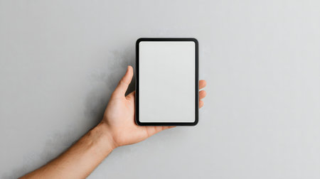 A hand holds a tablet with a blank white screen against a gray background. Perfect for mockups.の写真素材