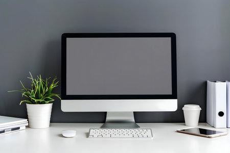 A clean and minimalist workspace with a modern desktop computer, keyboard, mouse, plant, tablet, and office supplies. The setup emphasizes efficiency and productivity.の写真素材