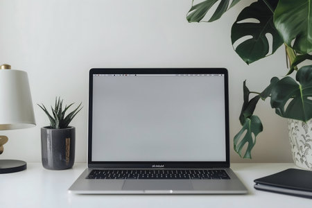 A minimalist workspace featuring a laptop, plants, and a lamp on a clean white desk.の写真素材