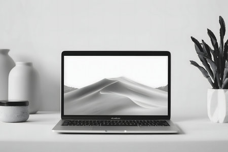 A grayscale image of a laptop displaying a desert landscape wallpaper, accompanied by minimalist decor.の写真素材