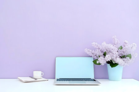 A serene workspace with a laptop, lilac flowers, and a cup on a pastel purple background.の写真素材