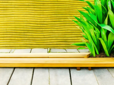 A wooden bench sits before a yellow bamboo wall, with vibrant green plants adding a touch of serenity.の写真素材