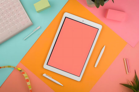 A flatlay image of a tablet, keyboard, and pastel stationery on a colorful desk. The vibrant colors create a cheerful and organized workspace.の写真素材