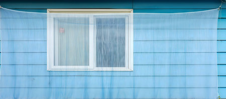 A light blue house with a window covered by sheer fabric.の写真素材