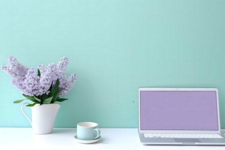 Lilac flowers in a vase beside a laptop on a mint green wall. Serene workspace aesthetic.の写真素材