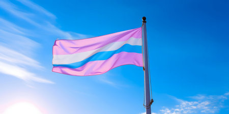 A transgender pride flag flies high against a vibrant blue sky, full of sun and hope.の写真素材