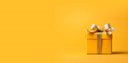 A single yellow gift box with a golden ribbon sits on a yellow background.の写真素材