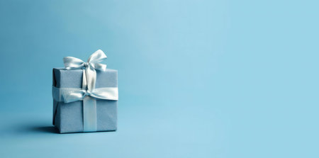 A single light blue gift box with a silver ribbon and bow sits on a matching blue background.の写真素材