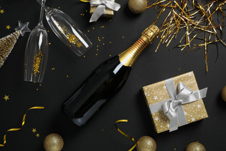 Bottle of champagne and Christmas decorations on black background, flat lay