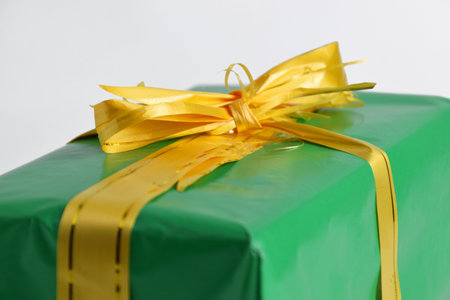 Green gift box with yellow ribbon and bow on white background, closeup