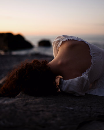 Beautiful young woman lying on a rock by the sea at sunsetの写真素材