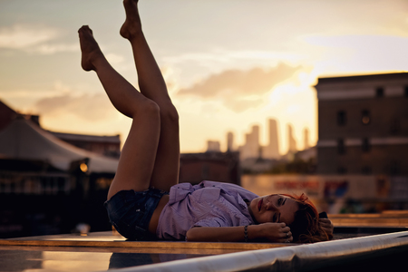 Beautiful Woman with red hair sitting on a roof or bridge, sunset lightの写真素材