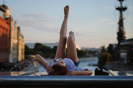 Beautiful Woman with red hair sitting on a roof or bridge, sunset lightの写真素材