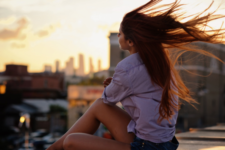 Beautiful Woman with red hair sitting on a roof or bridge, sunset lightの写真素材