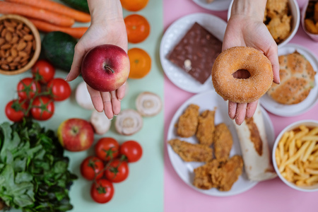 Concept photo of healthy and unhealthy food. Fresh vegetables and fruits against junk food, fast food on green and pink backgroundの写真素材