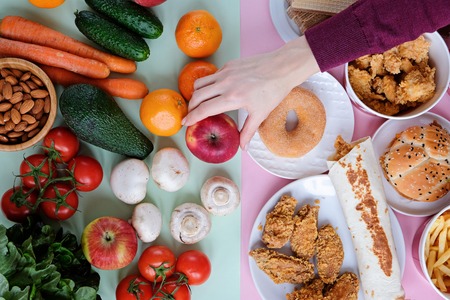 Concept photo of healthy and unhealthy food. Fresh vegetables and fruits against junk food, fast food on green and pink backgroundの写真素材