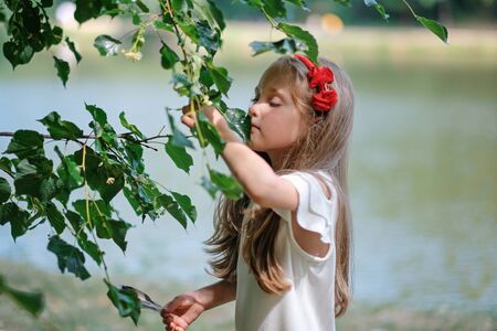 Portrait of beautiful little girl with long blond hair in white dress, smelling blossomの写真素材