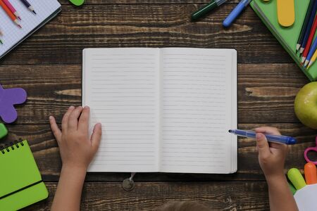 Back to school concept, creative layout with with various school supplies and stationery on wooden table. Kid's hands. Flat lay style composition, view from aboveの写真素材