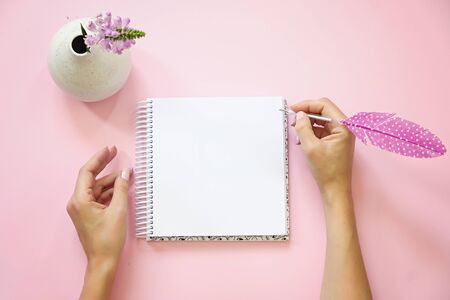 Womans hands holding pen with feather and notepad as mockup for your design. Pink background, flat lay style.の写真素材