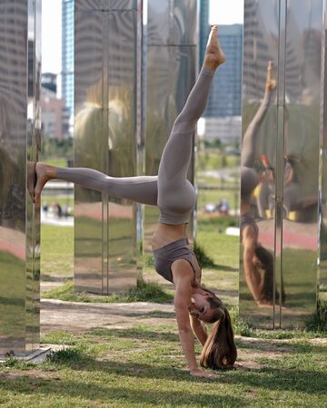 Young woman doing yoga exercises with city on background. Beautiful asana on hands