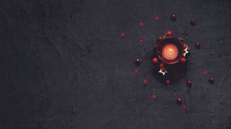 Black festive background with red decoration and candle, Chrtistmas and new year greeting card with place for textの写真素材