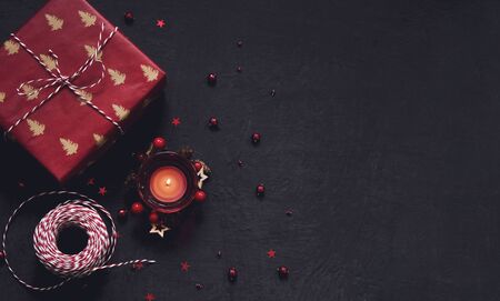 Black festive background with red decoration, candle and gift, Chrtistmas and new year greeting card with place for textの写真素材