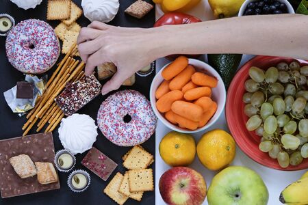Healthy and unhealthy food concept, fruits and vegetables vs donuts, sweets and chocolate with womans hand. Top viewの写真素材