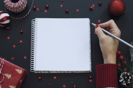 Note pad on black festive background with red decoration. Chrtistmas and new year concept, place for...