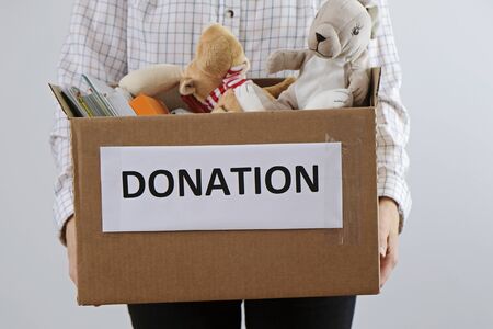 Donation concept: woman holding box full of books and toys. Donate for children please