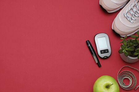 Flat lay with diet diabetes weight loss concept - Sneakers, tape measure, glucometer on a red background, place for textの写真素材