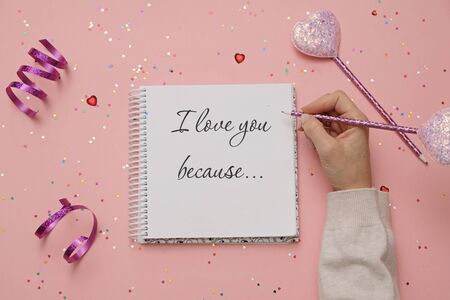 Valentine day composition with hearts, woman's hand and notebook on festive pink background. Flt lay