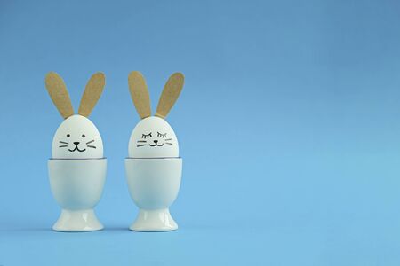 Blue Easter background with copy space - two white eggs decorated like rabbits.
