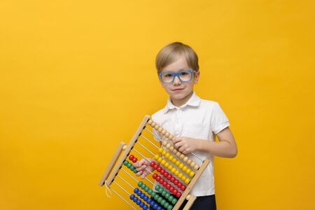 Cute little school boy in glasses holding scores on yellow background, copy space. Math conceptの写真素材