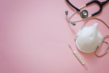 Pink background about pandemia of corona virus with stethoscope, medical mask and thermometer with...