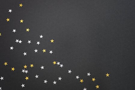Festive black background with silver and gold star confetti, empty space