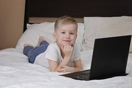 Cute boy kid and laptop lying on the bed while quarantine of corona virus. Distance education, stay...