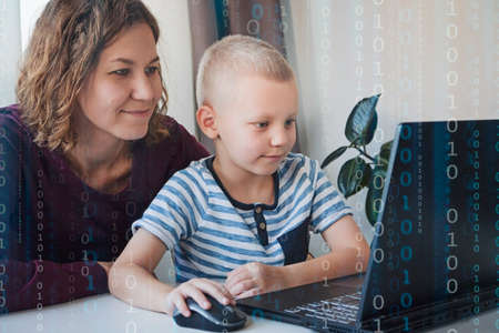 Young programmer writing code on a computer together with his mom or teacher. Programming lessons...