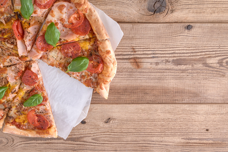Delicious fresh pizza with ham and tomato on a wooden background. Top view.の写真素材